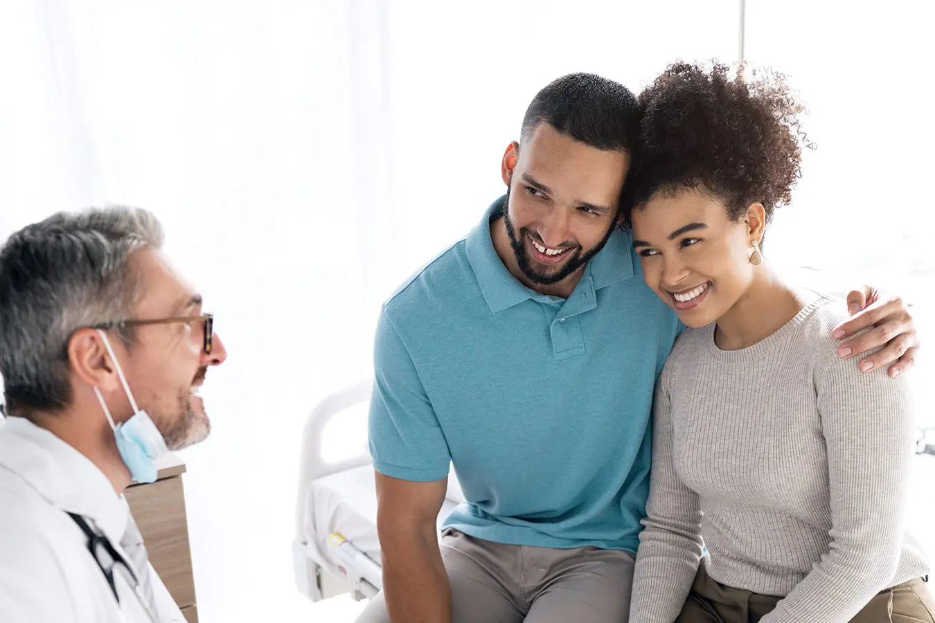 couple smiling with arm around each other waiting for results from doctor holding clipboard