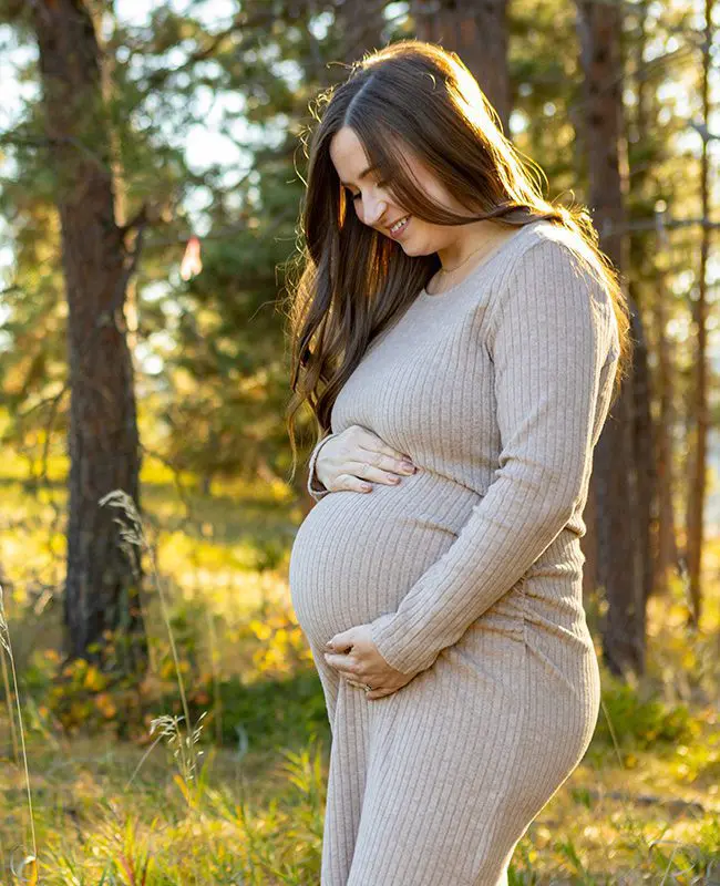 a pregnant woman smiles while placing her hands on her stomach