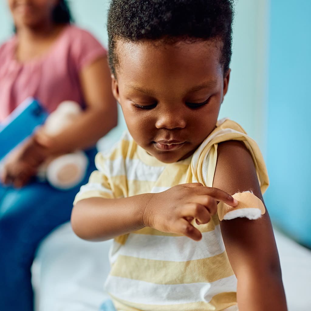 a young child points to a band aide on their arm