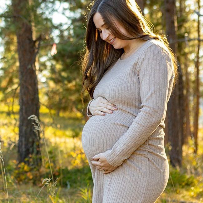 a pregnant woman smiles while placing her hands on her stomach